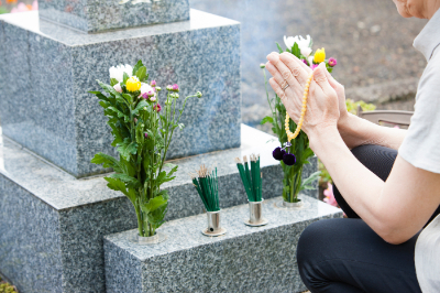 墓前に花を供え手を合わせる遺族